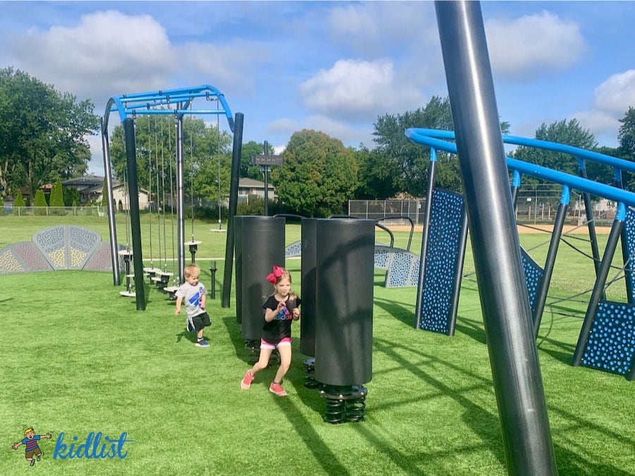 Kids running through a ninja park's obstacles. The park has artificial turf.