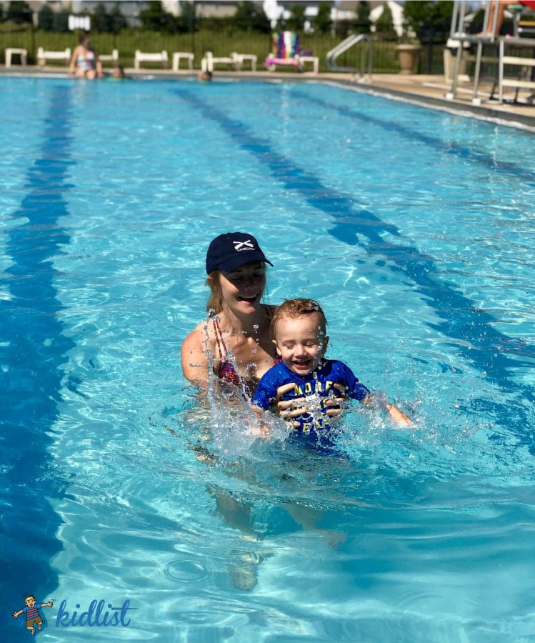 pool membership near me, mom and baby boy standing in between two lanes in a lap pool smiling and splashing