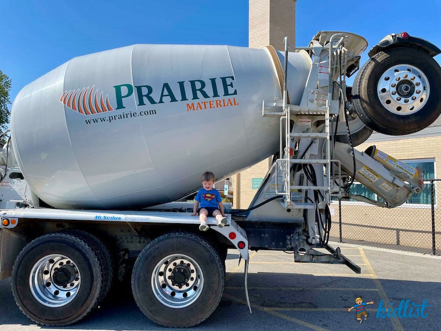 Young child sitting on a concrete mixer at a Touch a Truck event.