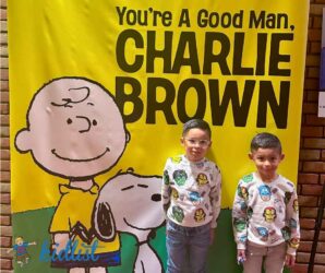Two children standing in front of a poster for You're a Good Man Charlie Brown at the Marriott Theatre.