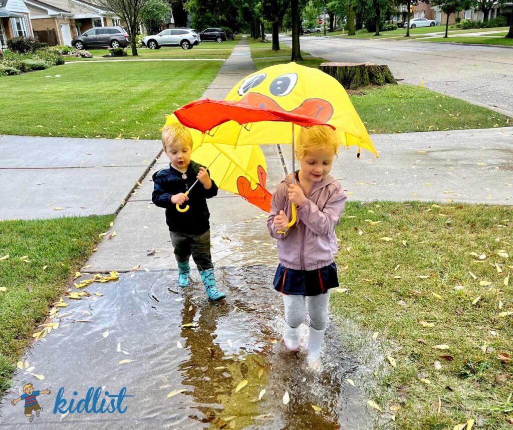 Two young children splashing in a puddle for rainy day activities
