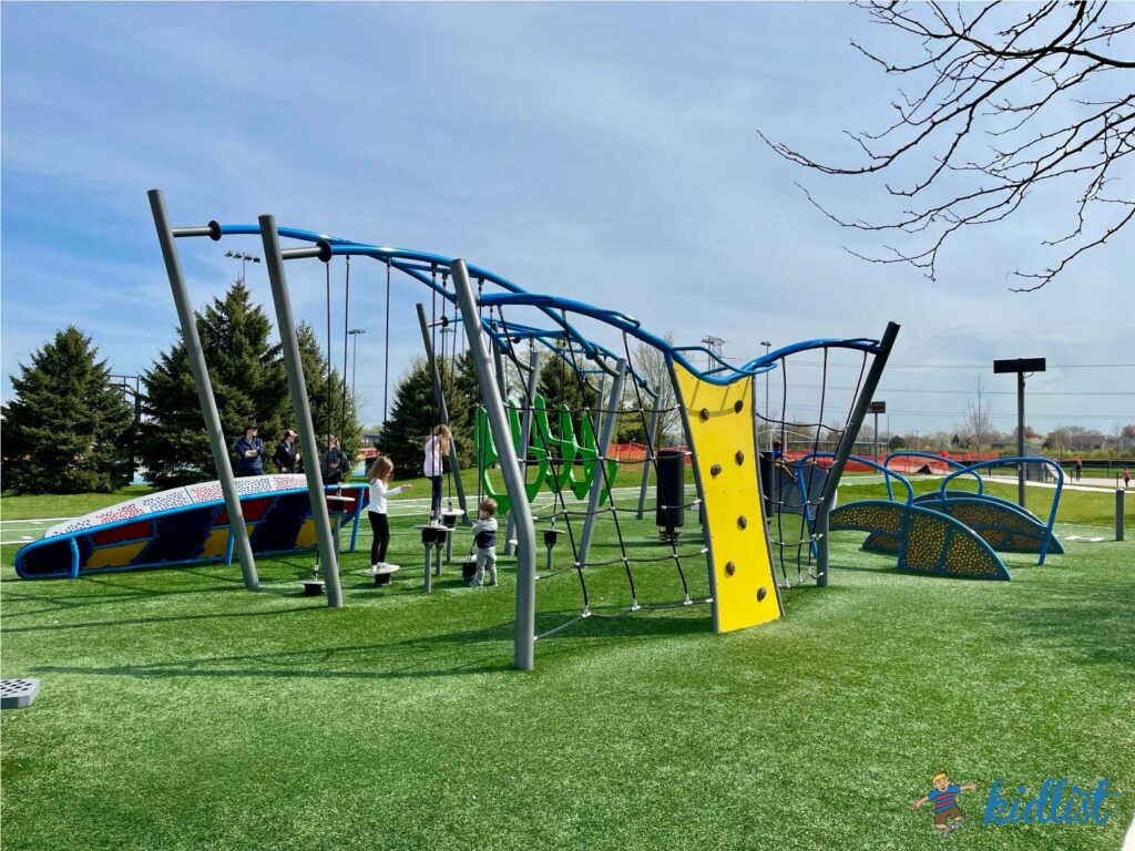 Climbing equipment and other obstacles on a ninja park with artificial turf.