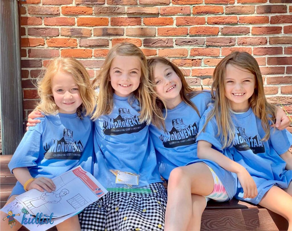 four girls with their arms around each other wearing vacation bible school t-shirts with smiles on their faces, ready to start VBS for the day