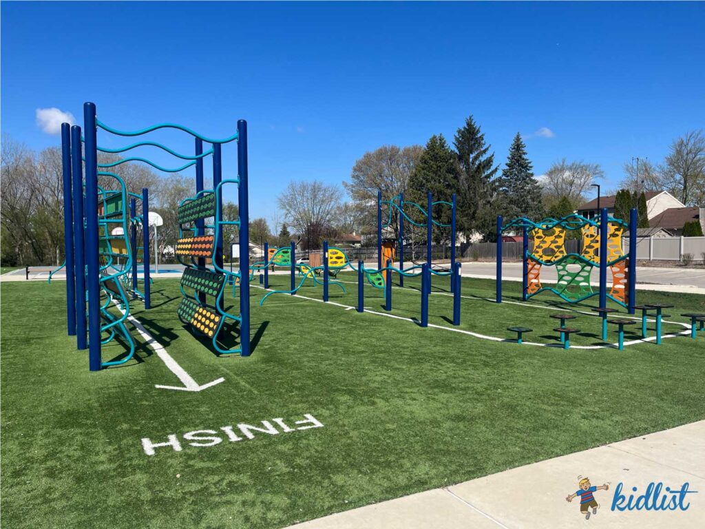 Ninja park equipment on artificial turf, with a line leading kids through the obstacles.