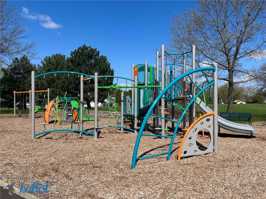 A new playground with woodchips, brightly colored play structures, and swings.