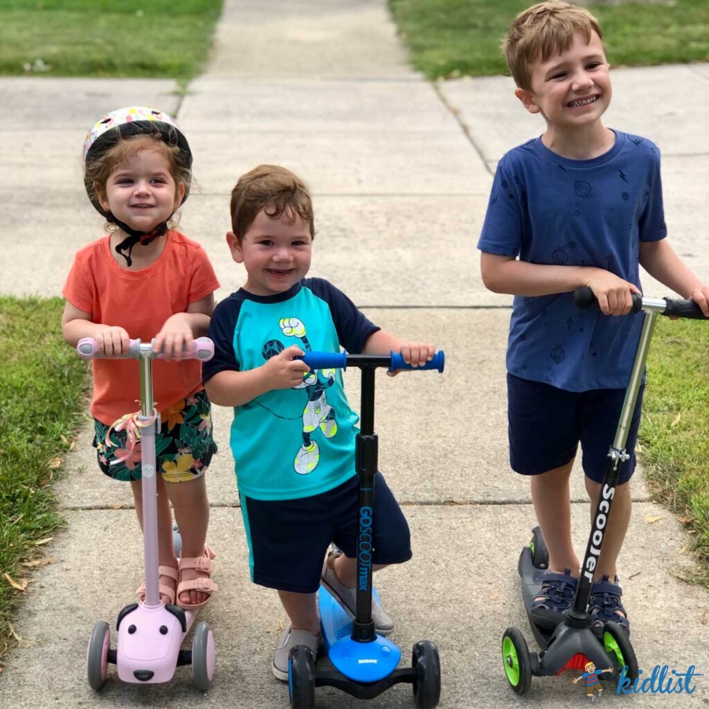 Three kids riding scooters down a sidewalk.