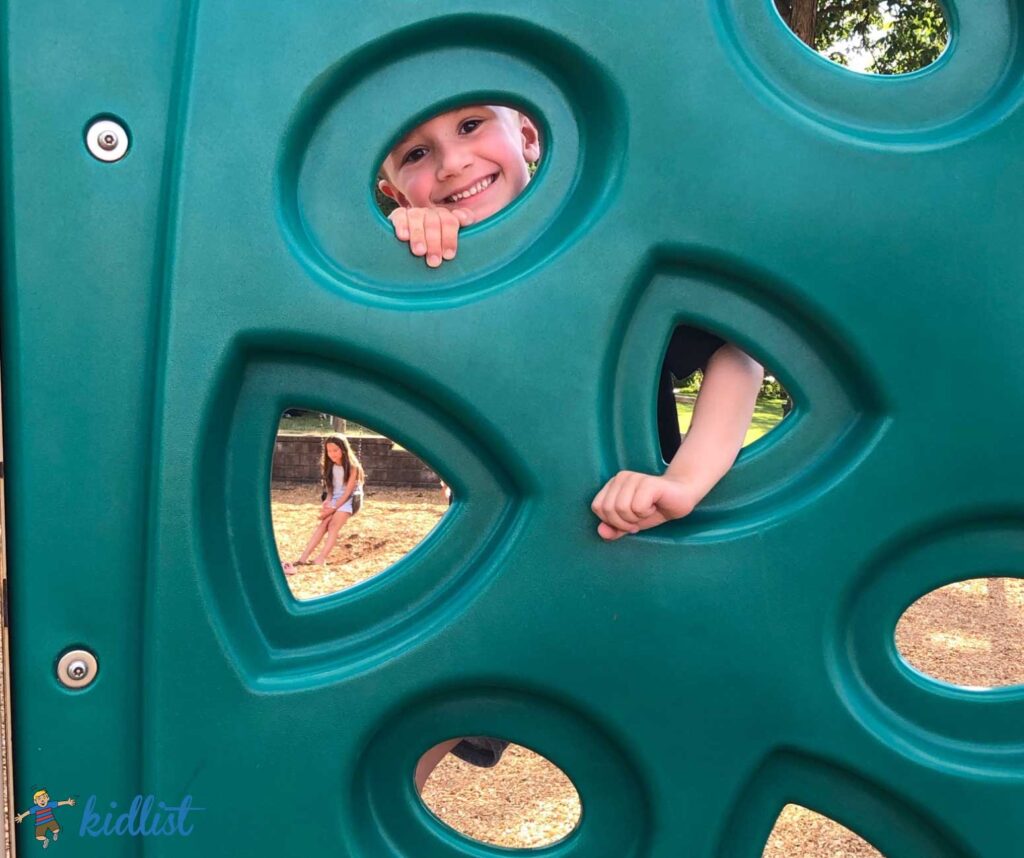 Child peeking out from a climber on a playground.