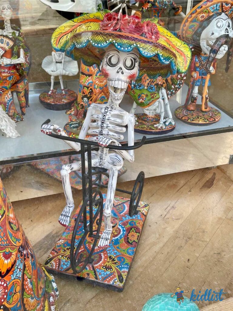 A shop display featuring a statue of a sugar skull-style skeleton on a bicycle.