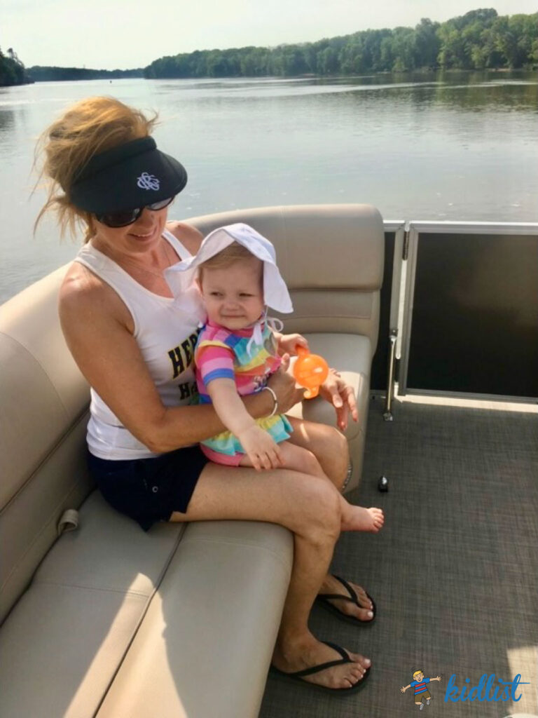 An adult holding a baby in a cute sun hat in a boat on a calm lake.