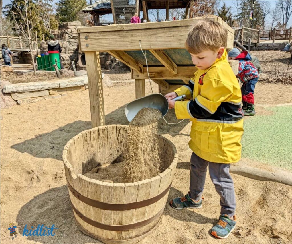 A child pouring sand into a bucket with a scoop.