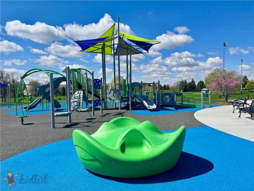 Playground with a spinner and other play structures on a soft, squishy surface.