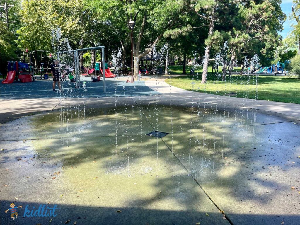 fountains of water springing up from the ground at Field Park in Oak Park with two playgrounds in the background