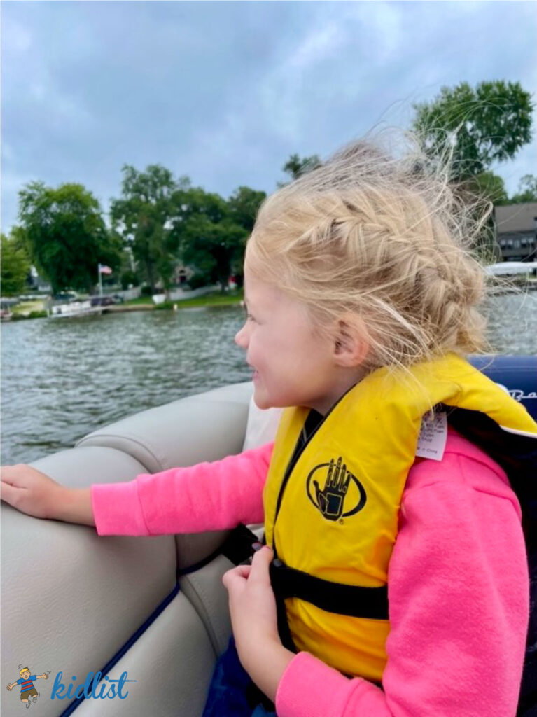 Child in a lifejacket on a boat enjoying the wind in their hair.