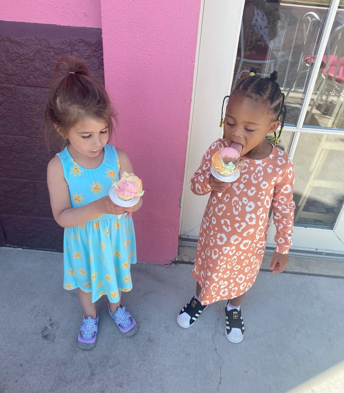 Two girls eating Rainbow Cones outside of a bright pink store.