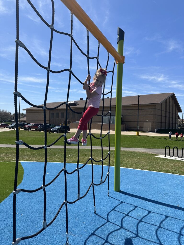Girl climbing on a net rope on the playground.