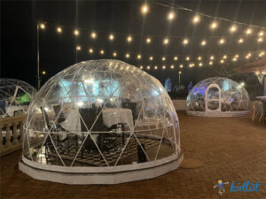 Greenhouse-style igloos with dining tables inside and outdoor lights strung overhead.