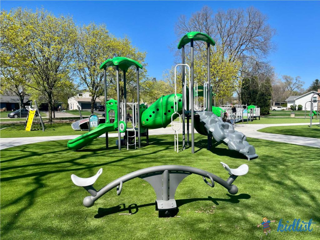 Kelly Park in Wheaton's playground with an artificial turf surface, see-saw, play structure, and more.