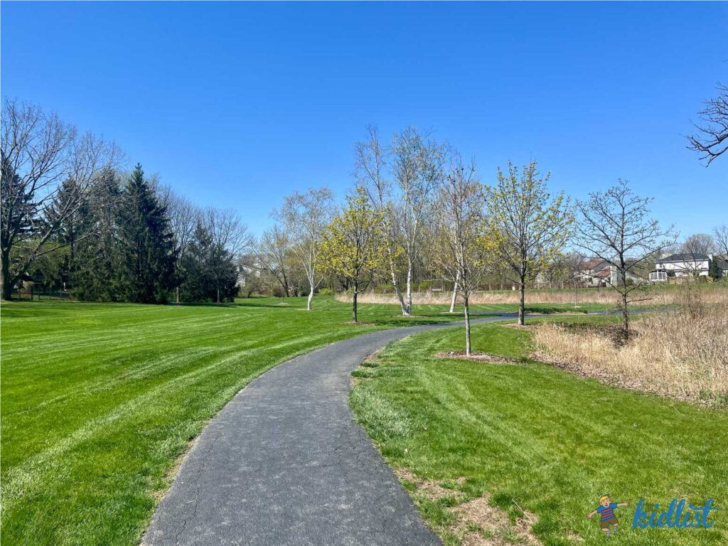Paved path through a grassy field at Mending Wall Park in Woodridge.