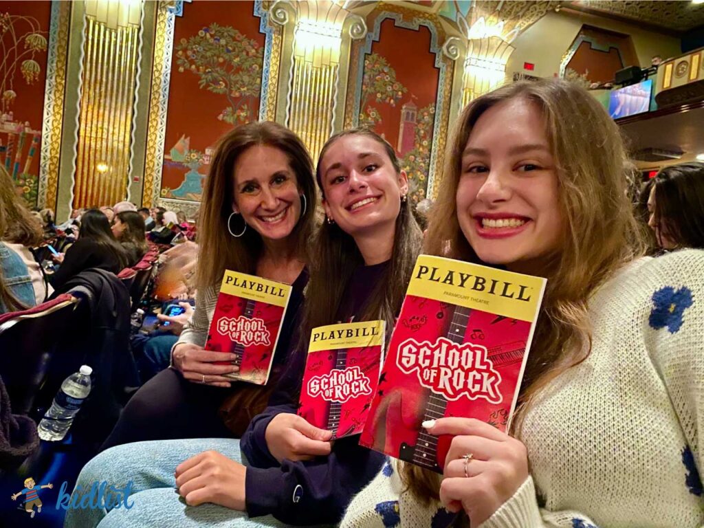 mom and daughters sitting in their theater seats, holding up their playbills for School of Rock at Paramount Theatre in Aurora
