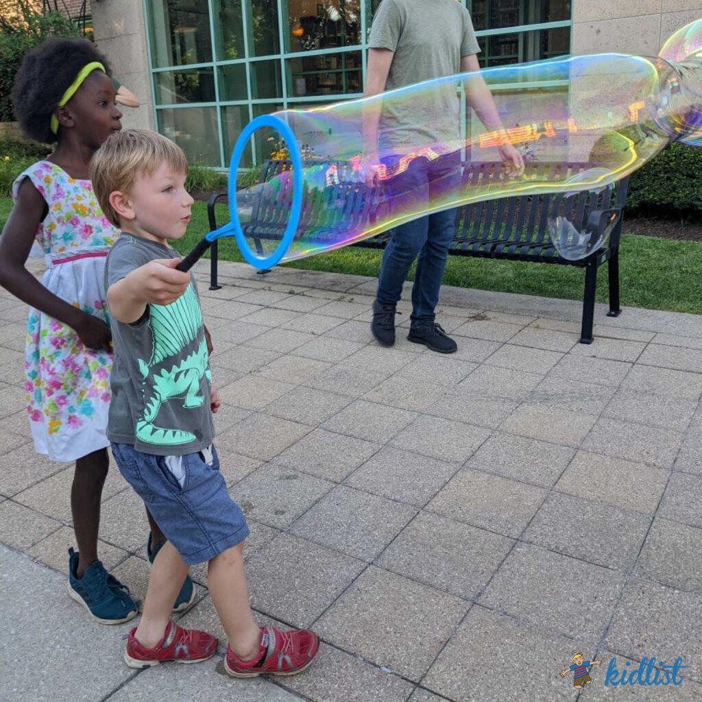 Children watch in amazement as they make giant bubbles with a bubble wand.