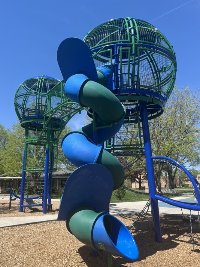 Orb-shaped play structures atop tall towers, connected by a bridge and with a spiral tube slide leading down from one.