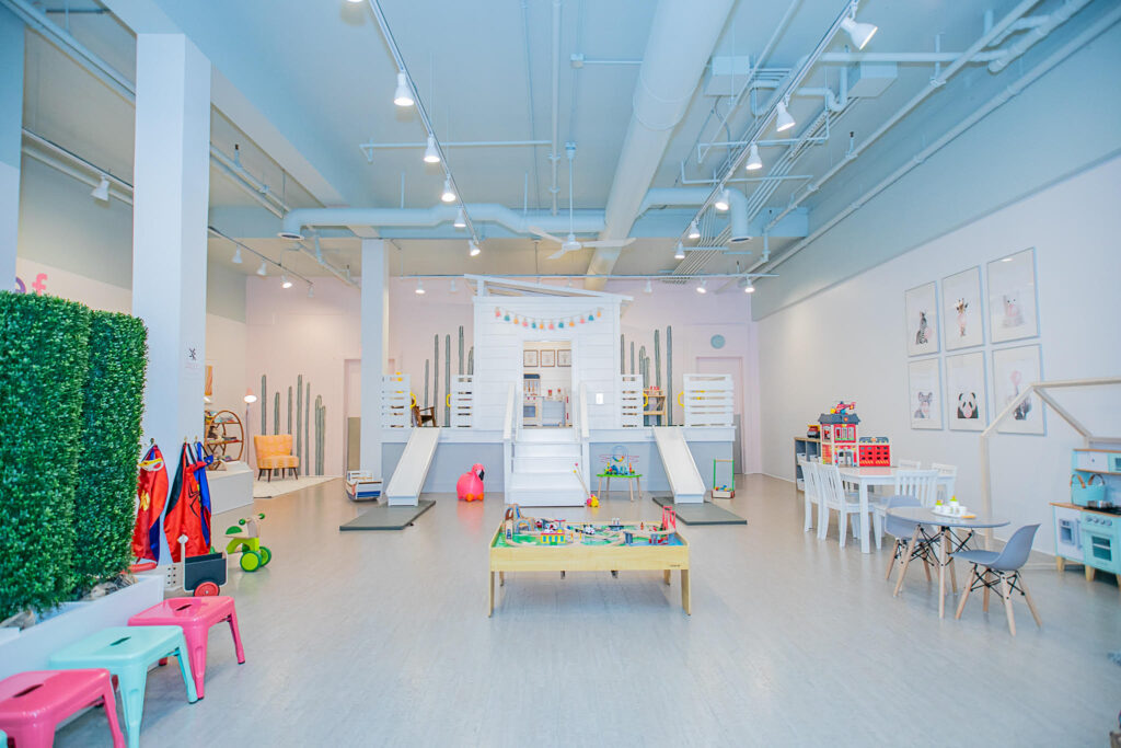 A bright, airy play space with a small climber with slides, train table, dress-up costumes, play kitchen, and other toys for toddlers and preschoolers.