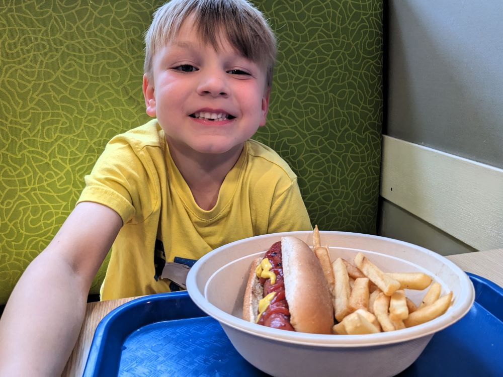 Child eating lunch at the Field Museum Explorer Cafe, with a big hot dog and French fries.